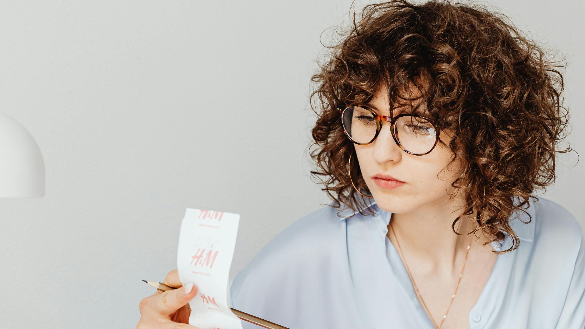 Curly-haired woman examining receipts with a calculator at her desk.