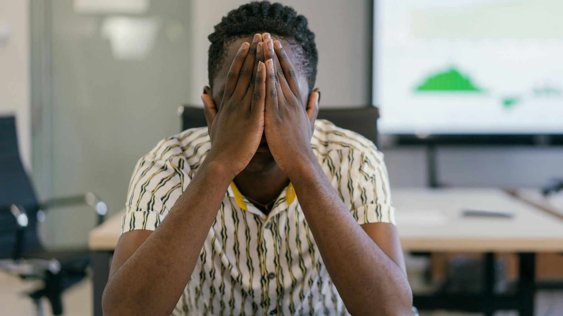 A stressed employee covering face in a modern office, depicting work pressure.