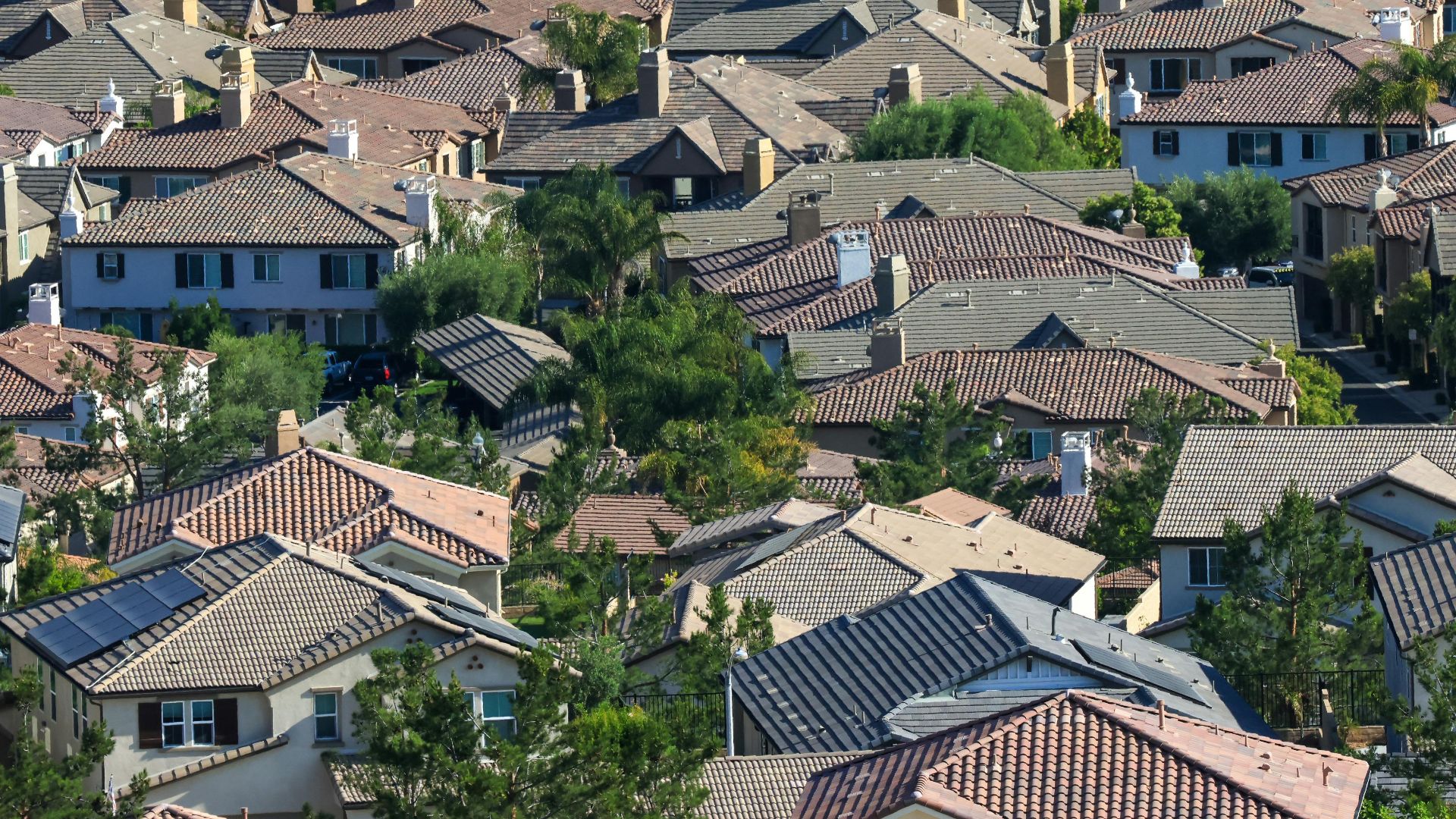 Aerial shot of a sunlit residential area showcasing tiled rooftops and lush greenery.