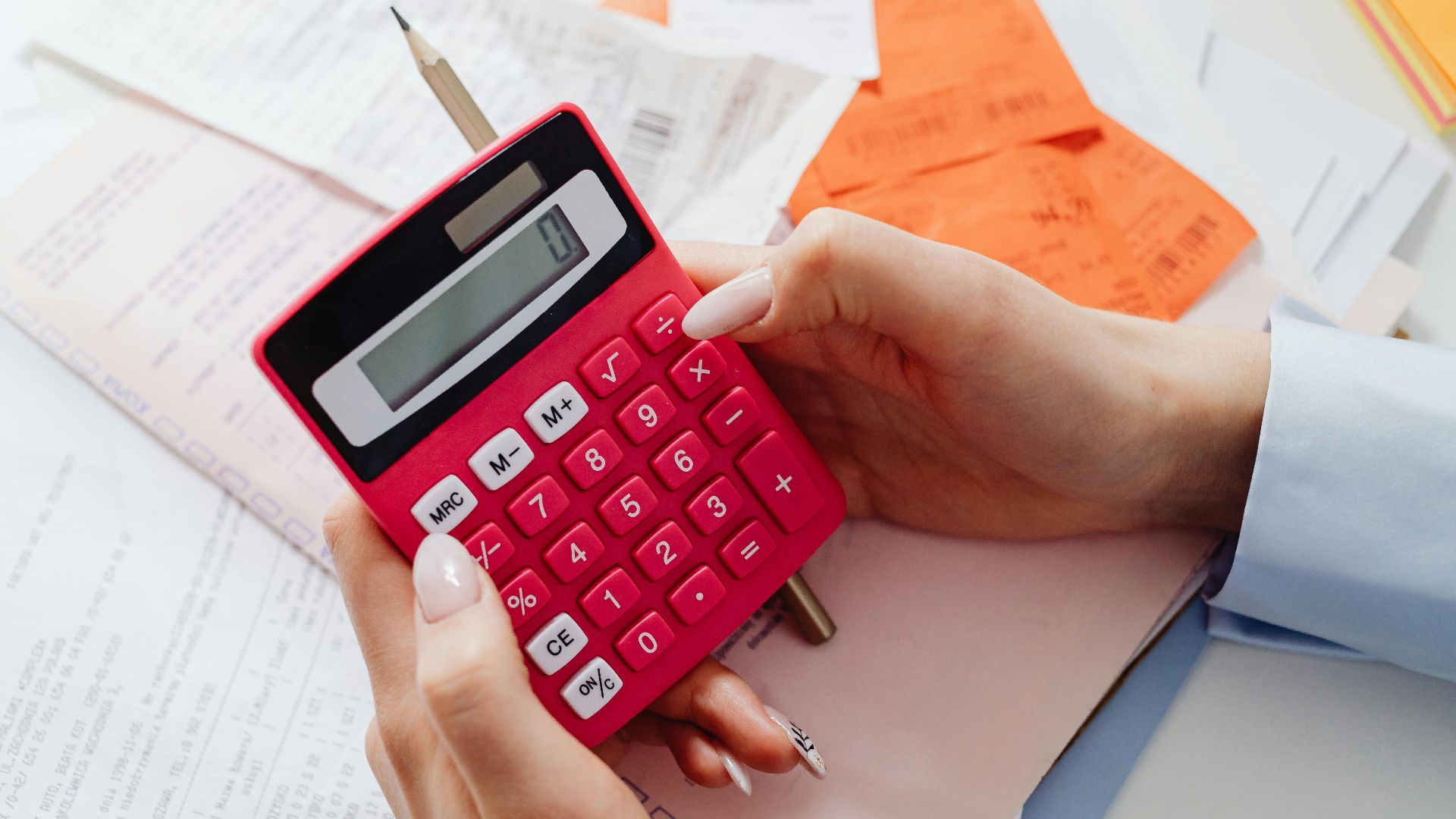 Close-up of hands holding a red calculator, managing finances with documents and receipts.