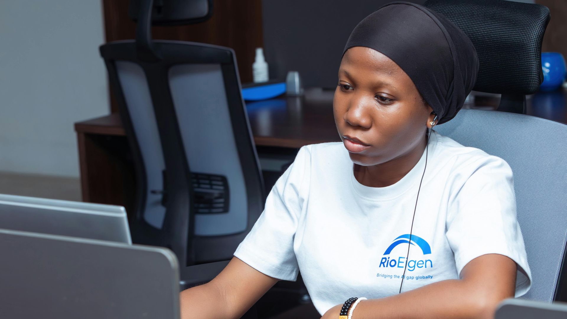 A young professional woman working on a laptop in a modern office environment.