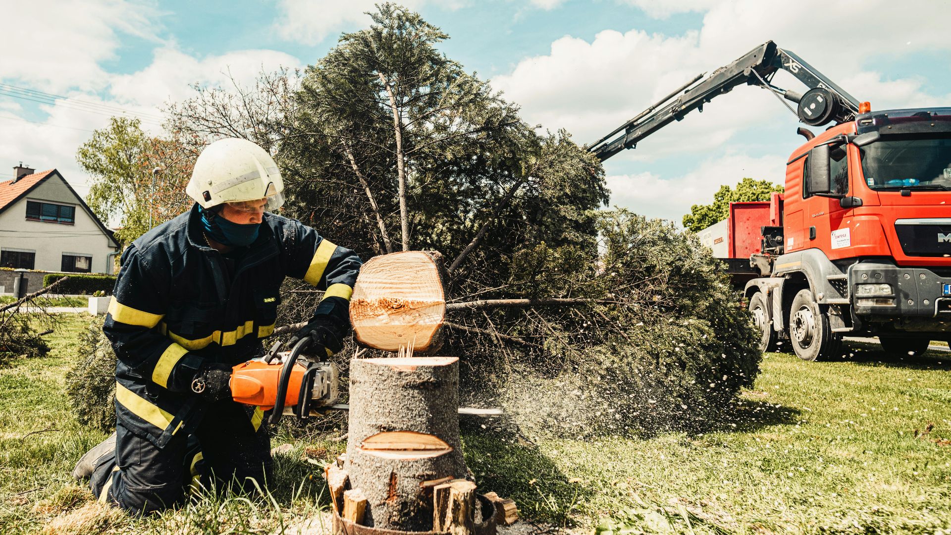 A firefighter uses a chainsaw to cut a tree stump while a truck assists in an outdoor setting.