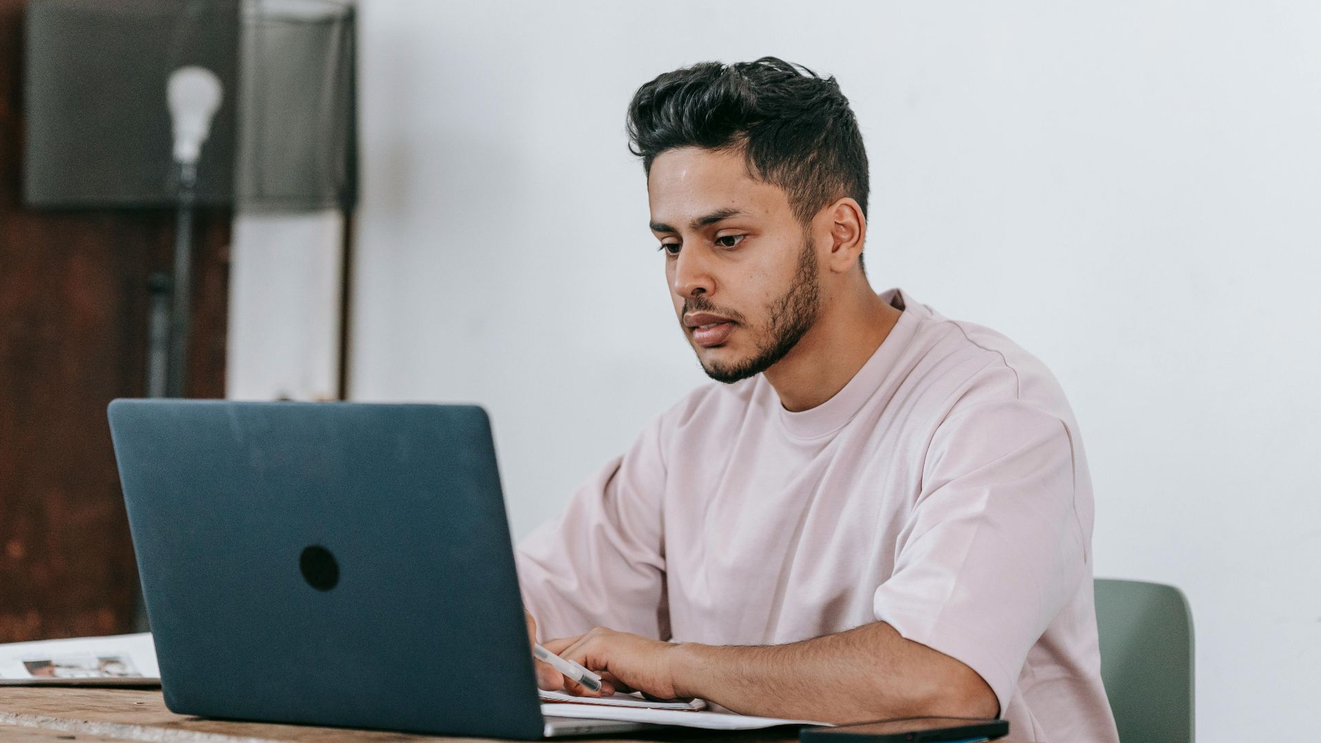 Focused young man working on a laptop in a minimalist home office setting.