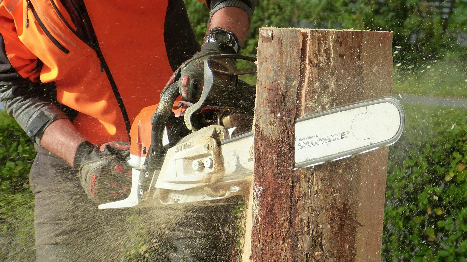 Lumberjack using a chainsaw to cut a tree trunk outdoors, showcasing professional equipment and safety gear.