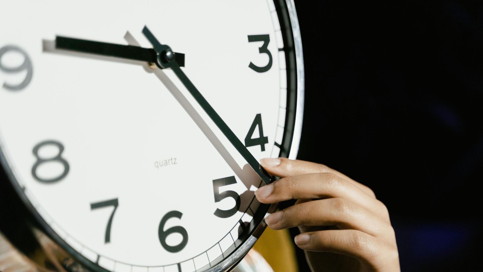 A hand adjusting the time on a large analog clock with bold numbers.
