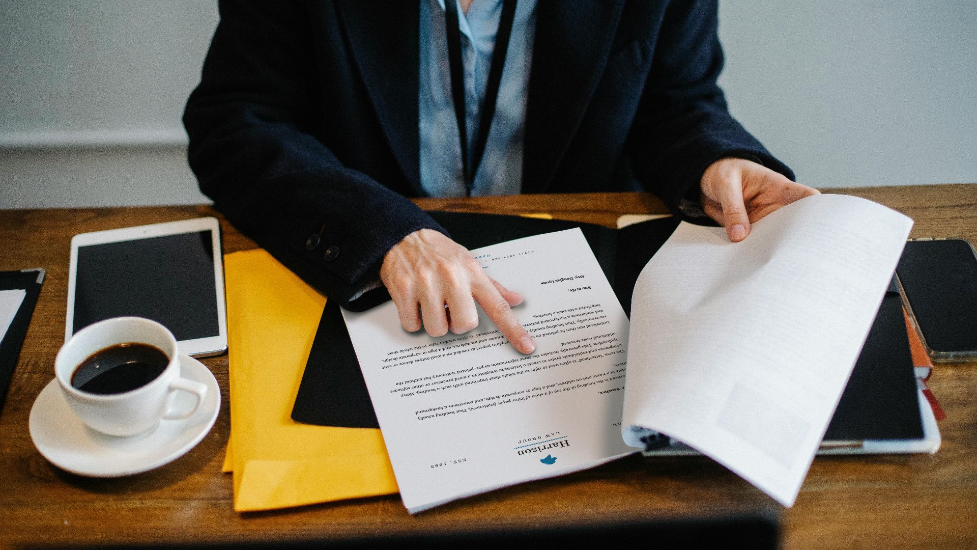 High angle of crop faceless woman in formal wear sitting at wooden table with tablet and coffee and reading documents