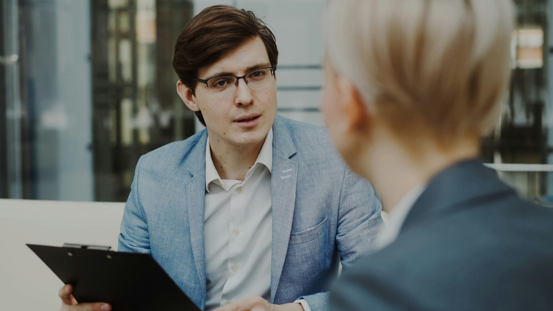 Man in suit holding clipboard talking to woman
