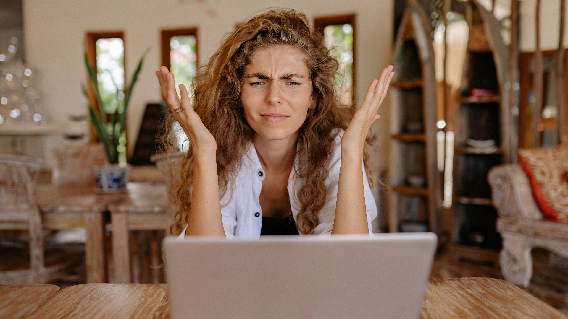 A woman frustrated with her laptop while working remotely indoors, expressing stress.