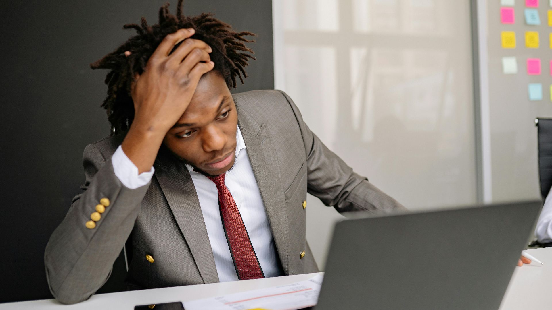 Businessman with dreadlocks looking worried while working on a laptop in the office.