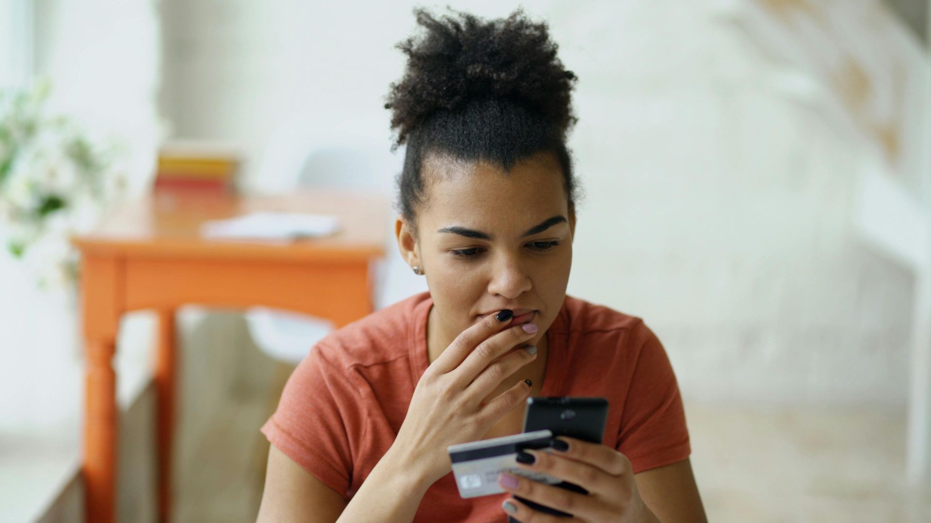 Young woman shopping online using a smartphone and credit card indoors.