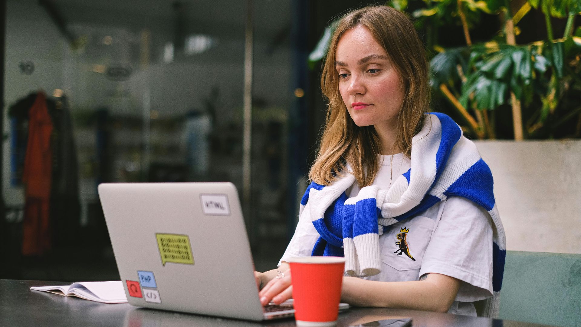 Young woman focused on laptop work in a modern cafe setting, surrounded by technology.