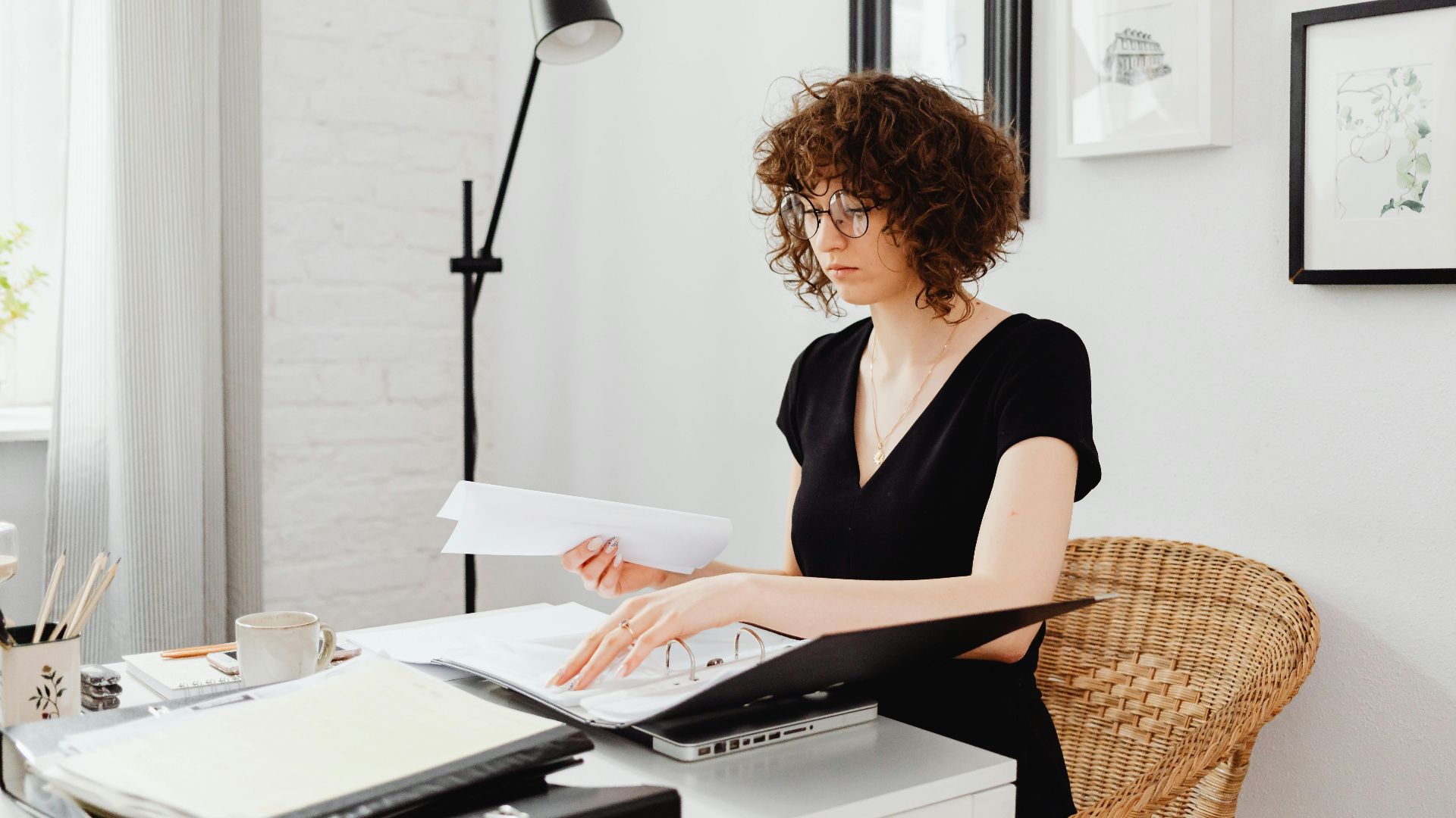 Caucasian woman with curly hair working at home office desk, organizing documents.