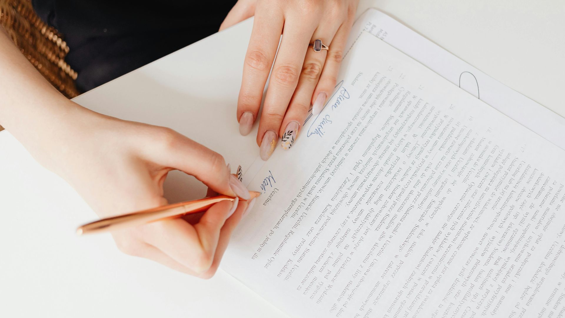 Close-up of woman's hands signing a legal document with elegant nail art using a pen.