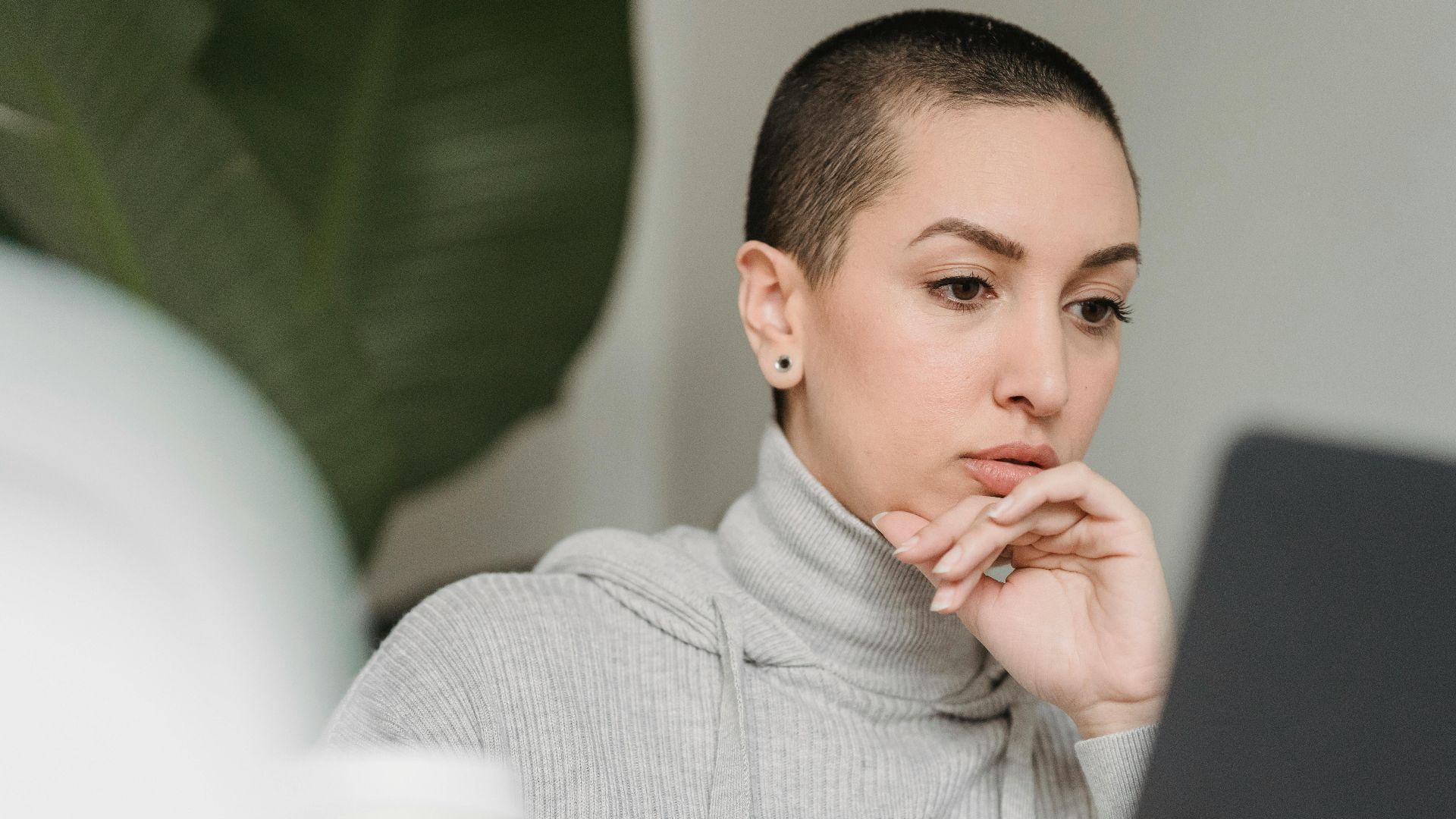 Woman with short hair concentrates deeply while working on a laptop indoors, emphasizing focus and modern work environment.