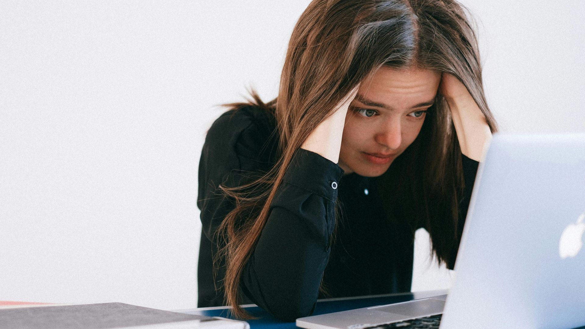 A stressed woman at a desk, looking at a laptop with a worried expression.
