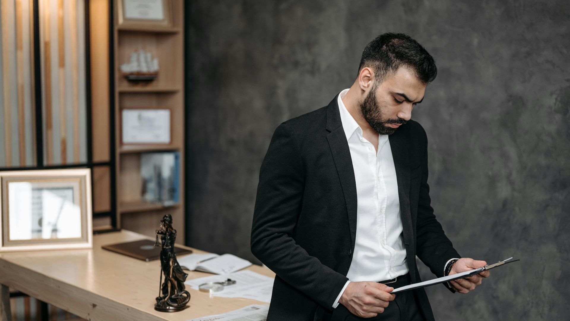 A male lawyer in a black suit focusing on paperwork in an office setting.