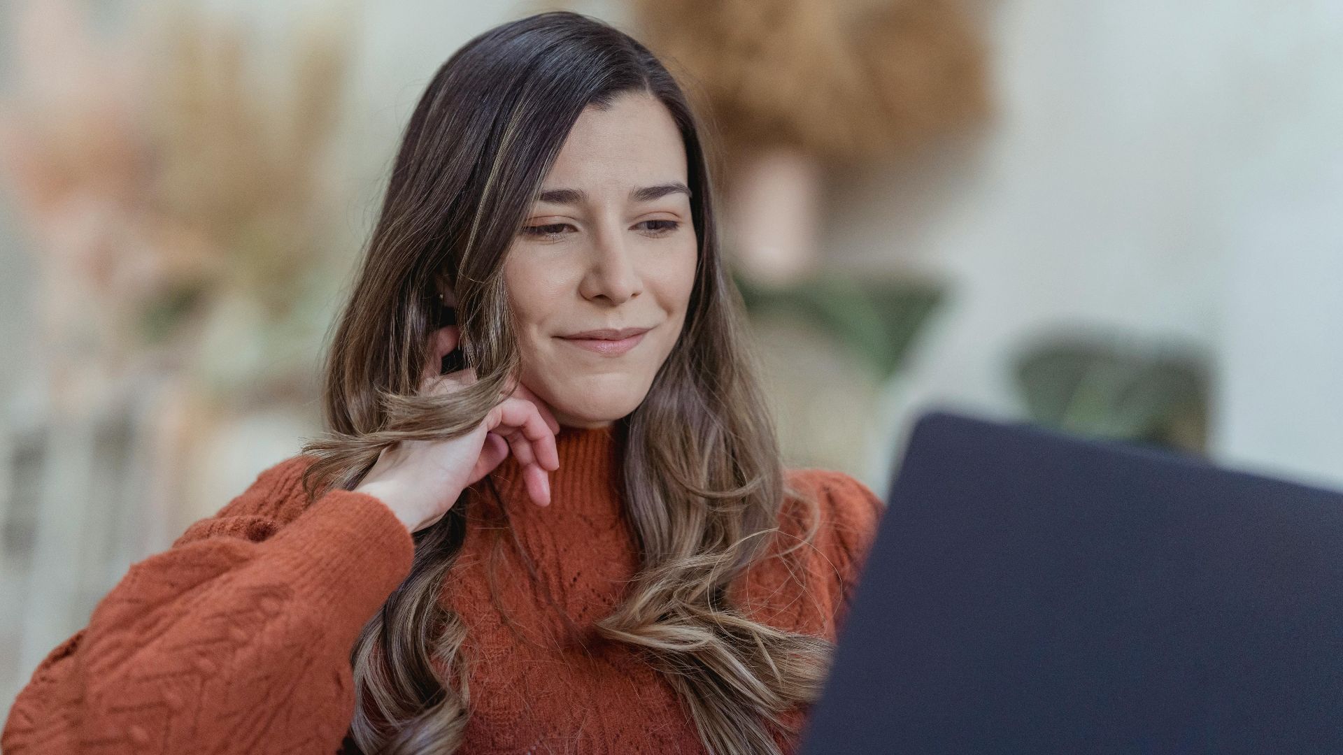 Woman in a sweater working on a laptop, exuding confidence and focus in a cozy, indoors setting.