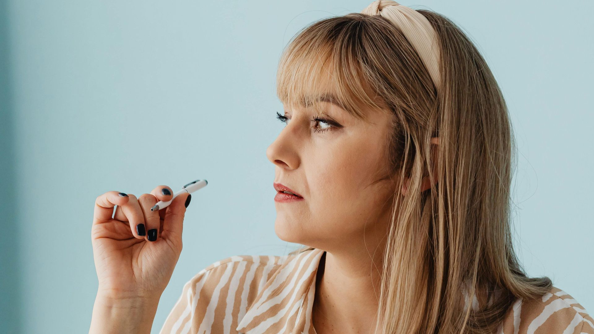 Portrait of a woman with blonde hair thoughtfully holding a pen in an office setting. Perfect for workplace themes.