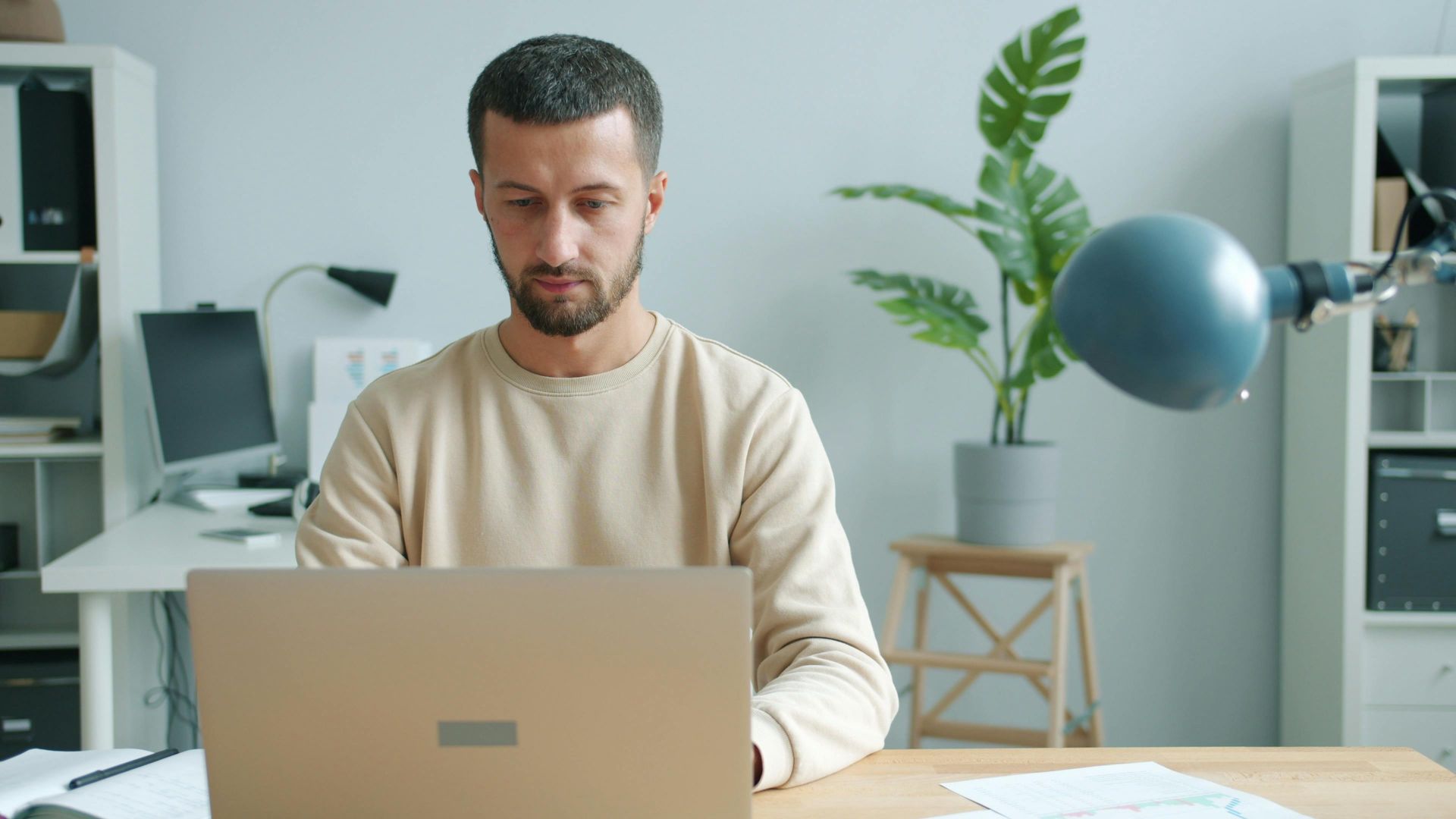 A man in a bright office environment focused on his laptop work.