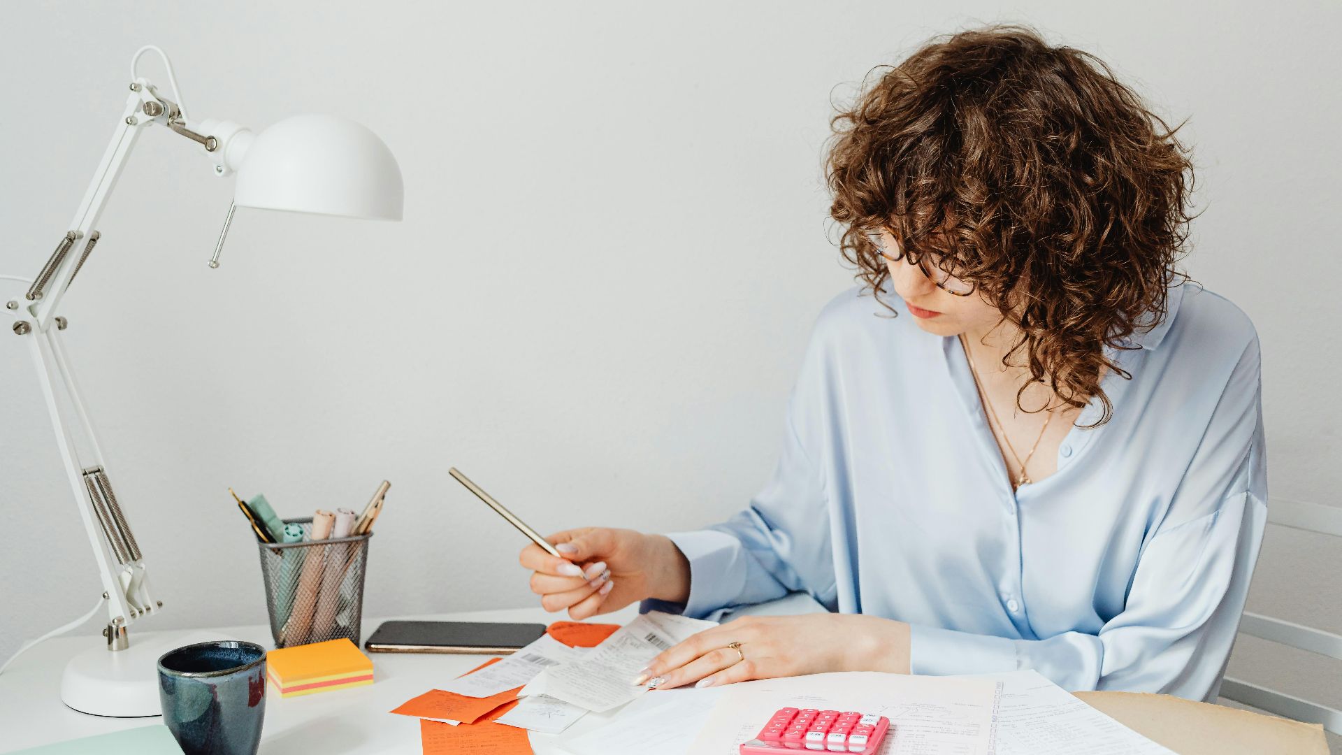 Woman in office calculating expenses with documents, calculator, and coffee.