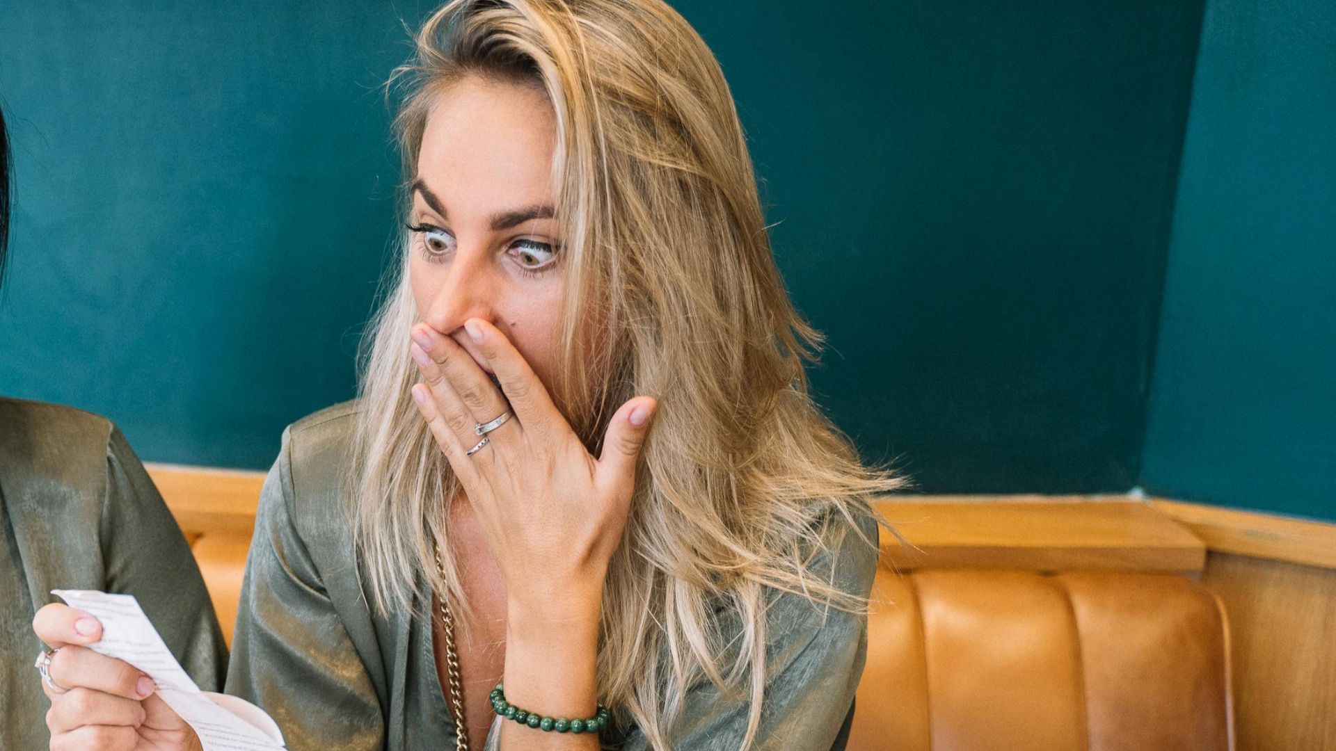 Two women express surprise while reviewing a restaurant bill in a casual setting.