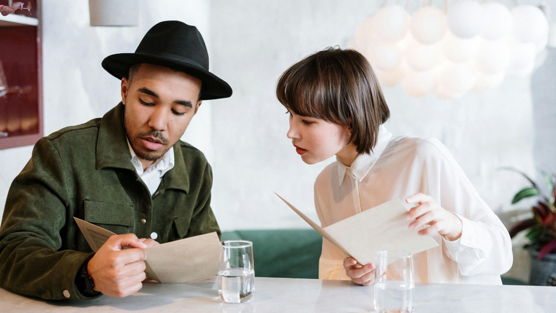 A couple reviews the menu in a modern cafe setting, discussing their meal choices.