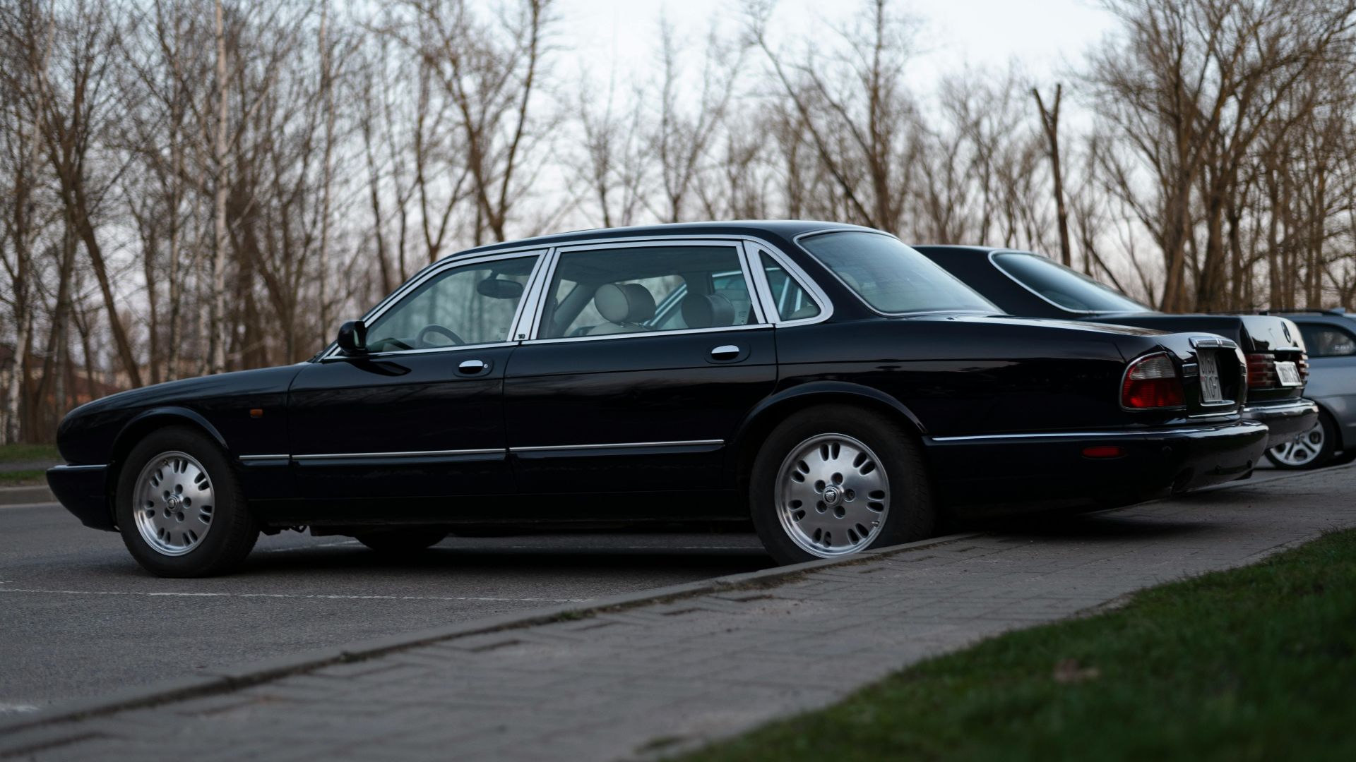 Elegant black Jaguar XJ8 parked outside on a sidewalk with trees in the background.