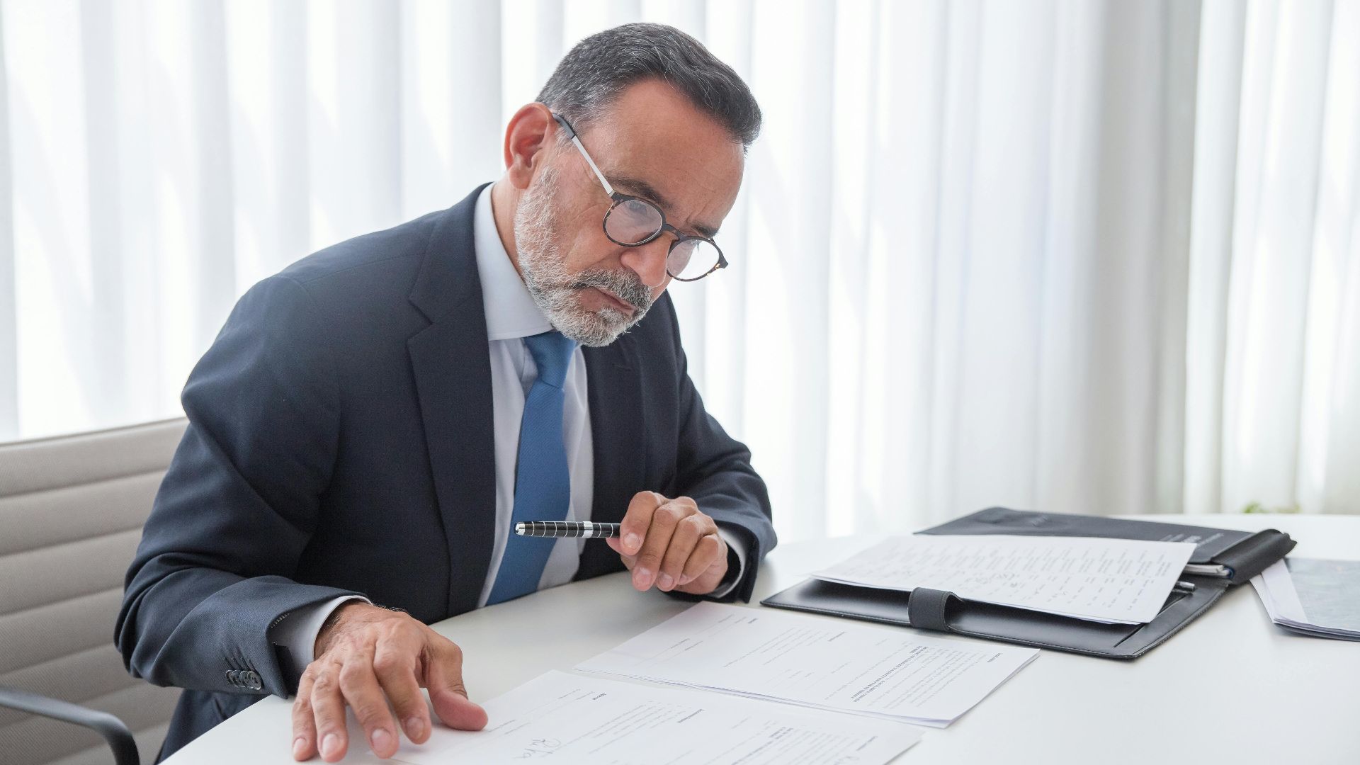 Elderly businessman focused on reviewing documents at his office desk.
