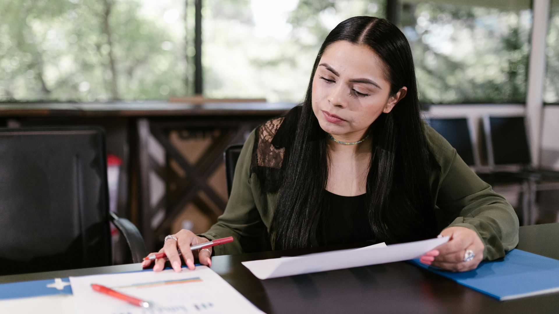 Professional woman in office setting studying documents with concentration.