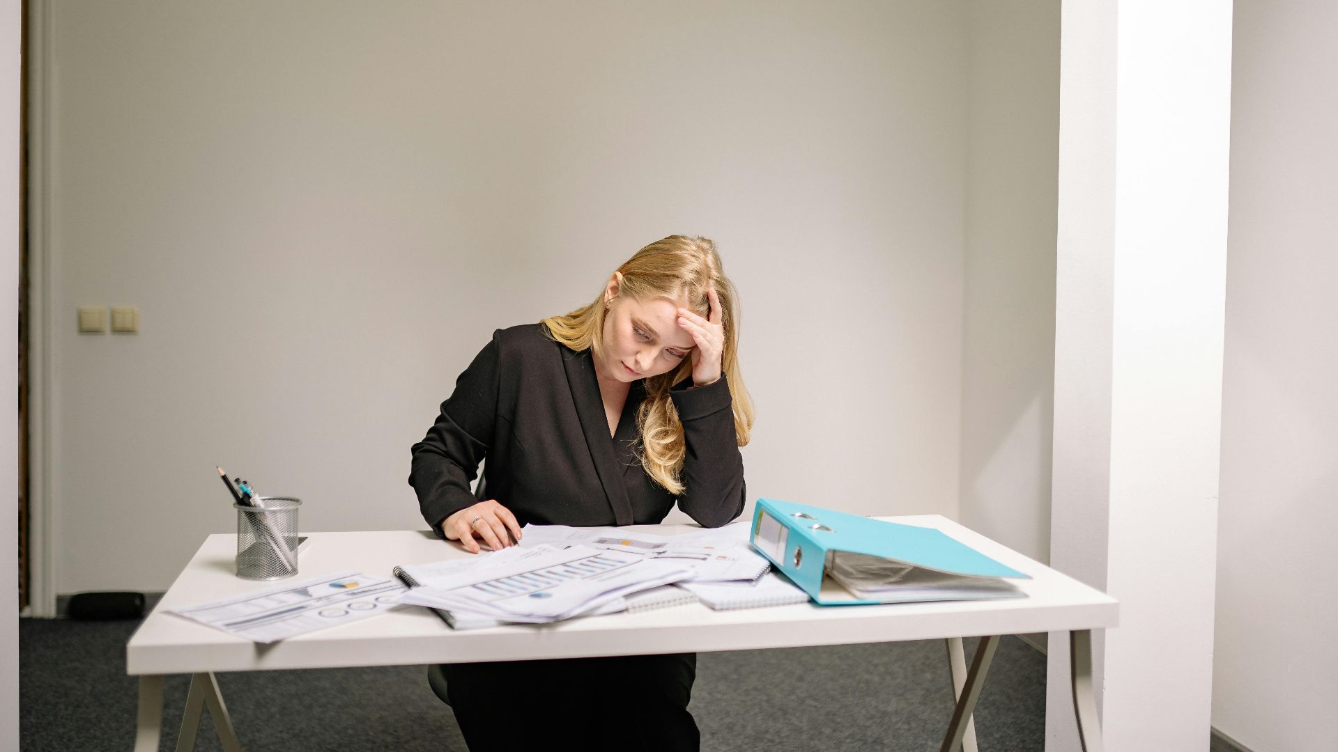 A stressed businesswoman reviewing documents at her desk, overwhelmed by paperwork.