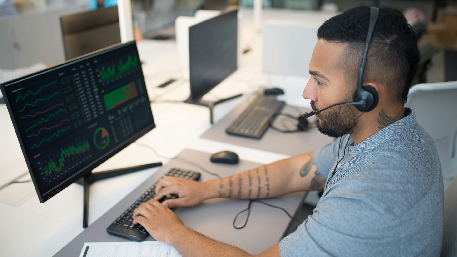 Man in a headset analyzing stock data on a computer monitor at his workspace.
