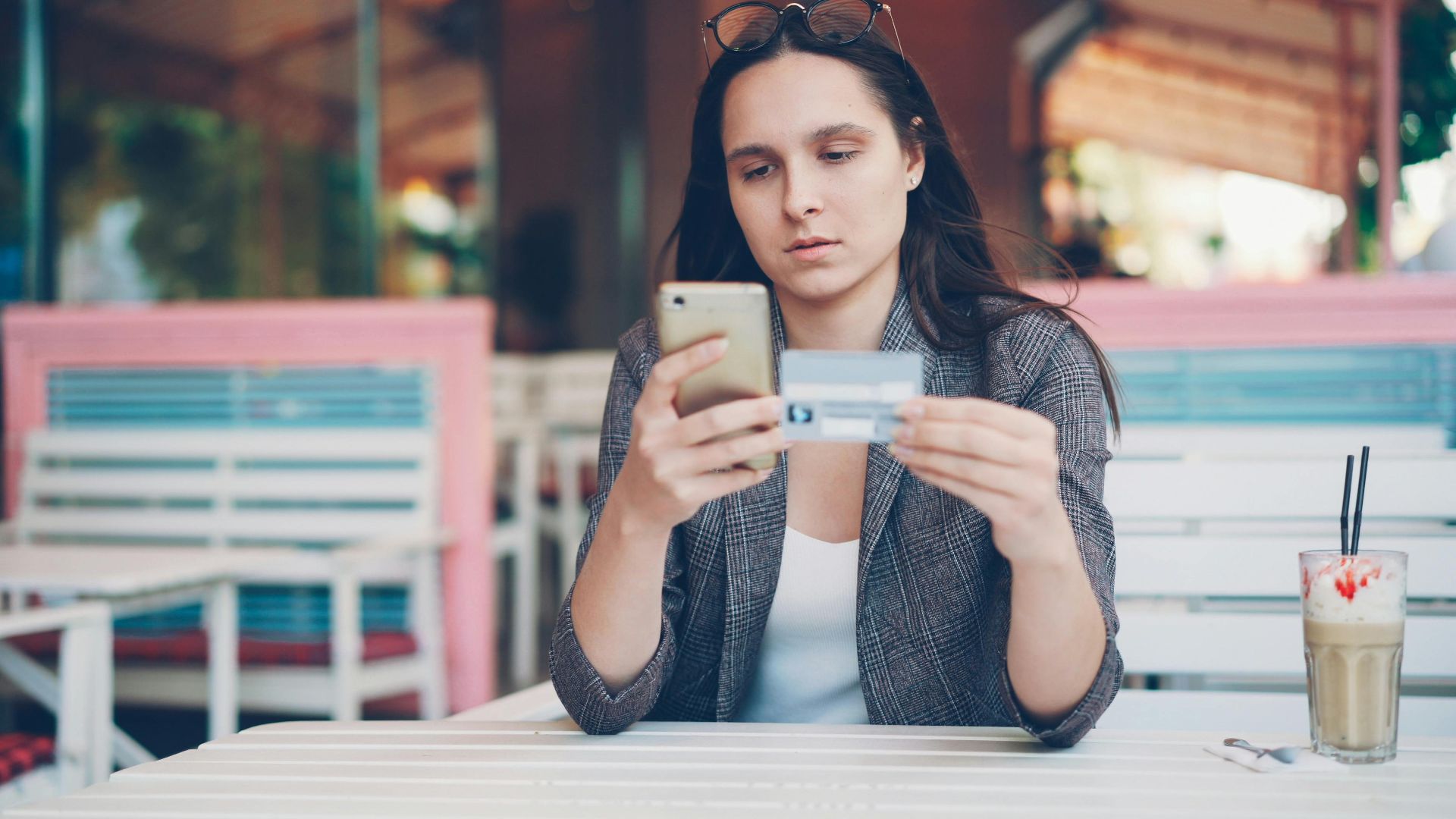 Woman using smartphone for online shopping at a cafe with credit card in hand.