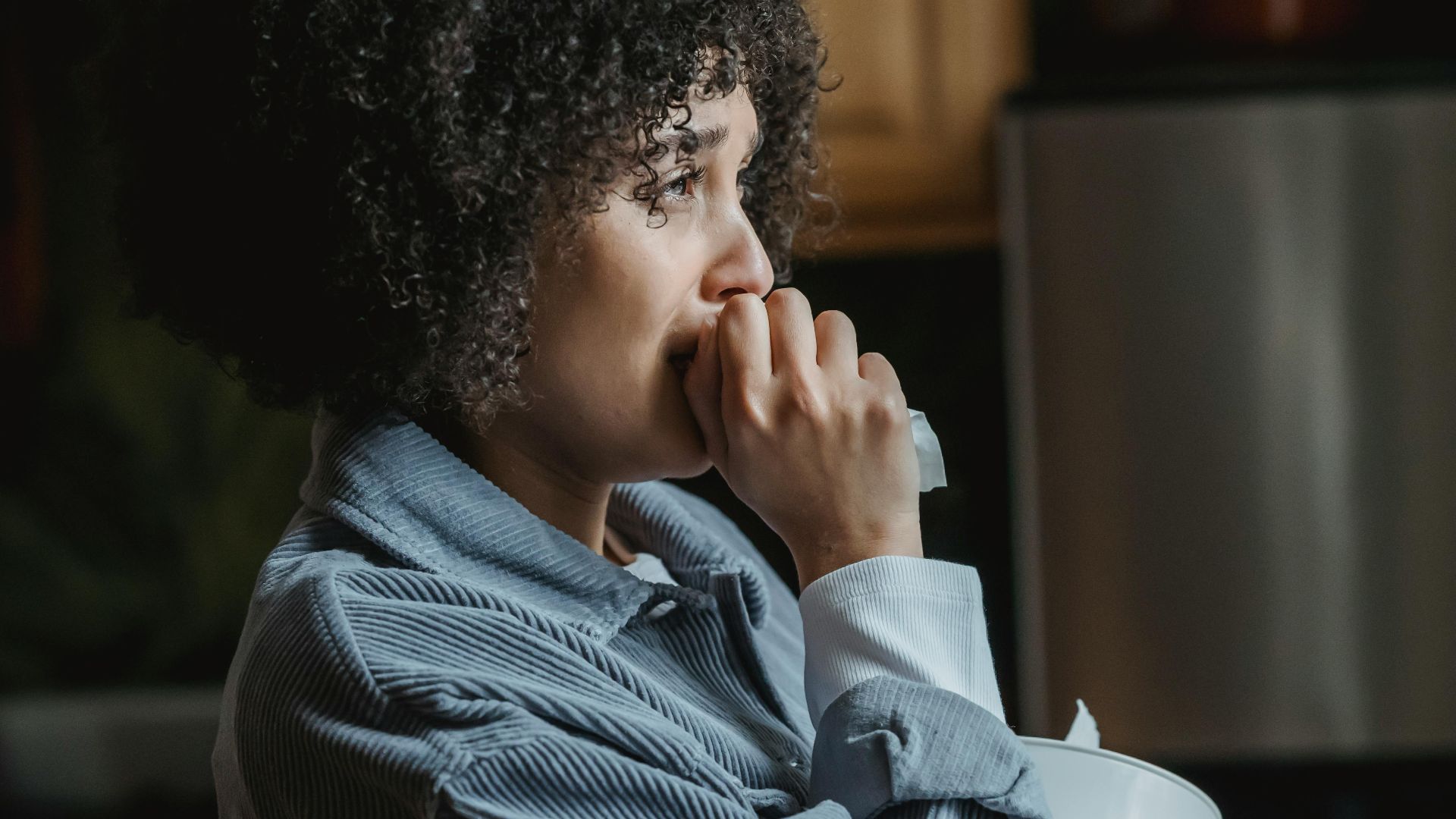 Side view of crying African American female with tissue sorrowing from unhappiness and grief in kitchen