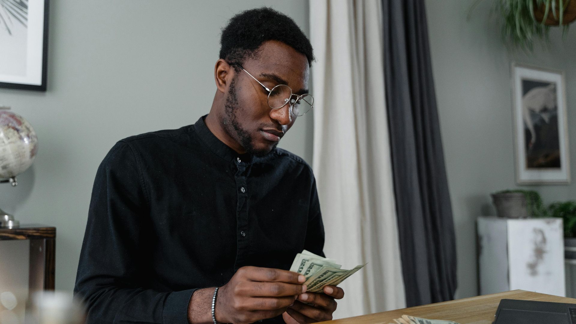 A focused man in glasses counting cash at a desk, indicating financial management.
