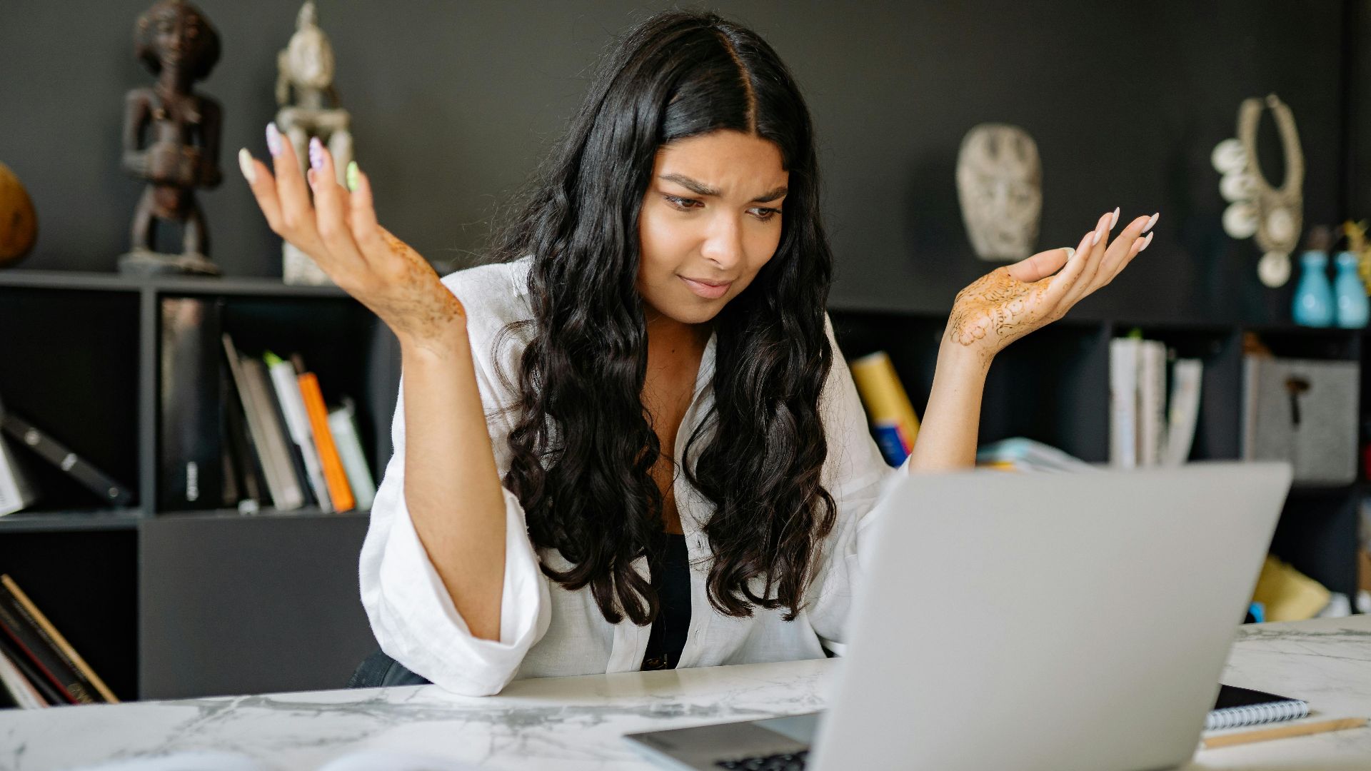 A woman at an office desk looks frustrated while working on her laptop. Modern office setting.