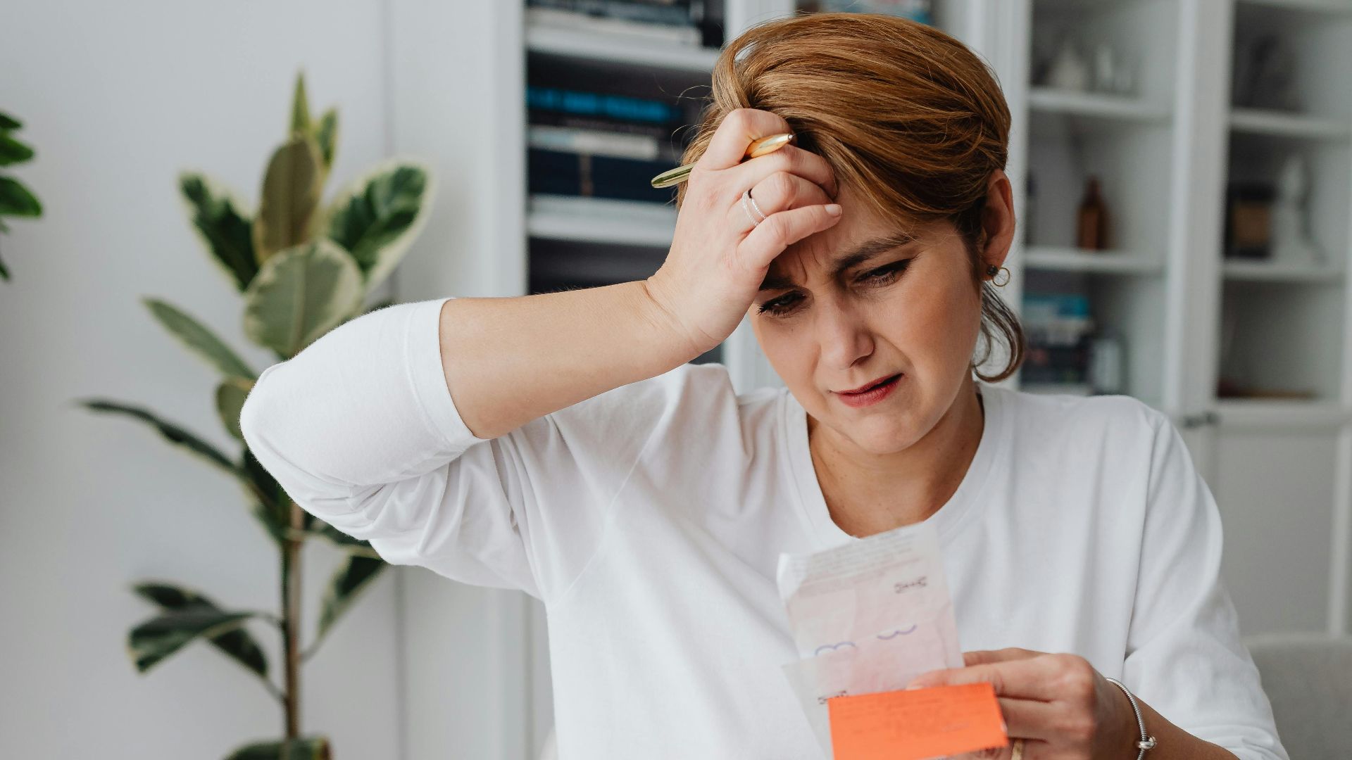 A businesswoman in an office looks frustrated while reviewing bills and finances with a laptop, displaying anxiety.