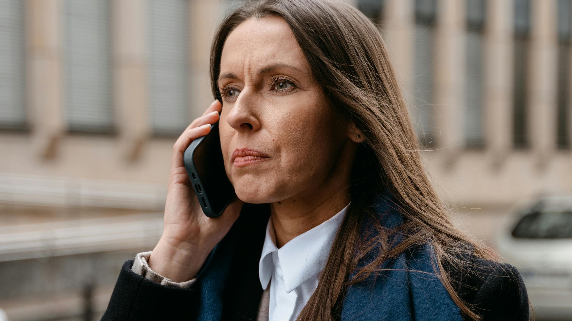 Confident woman in business attire talking on phone while walking in urban setting.