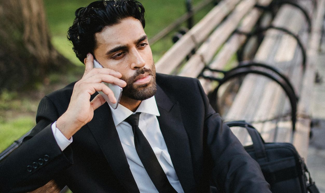 Man in Black Suit Sitting on Bench Speaking on Phone