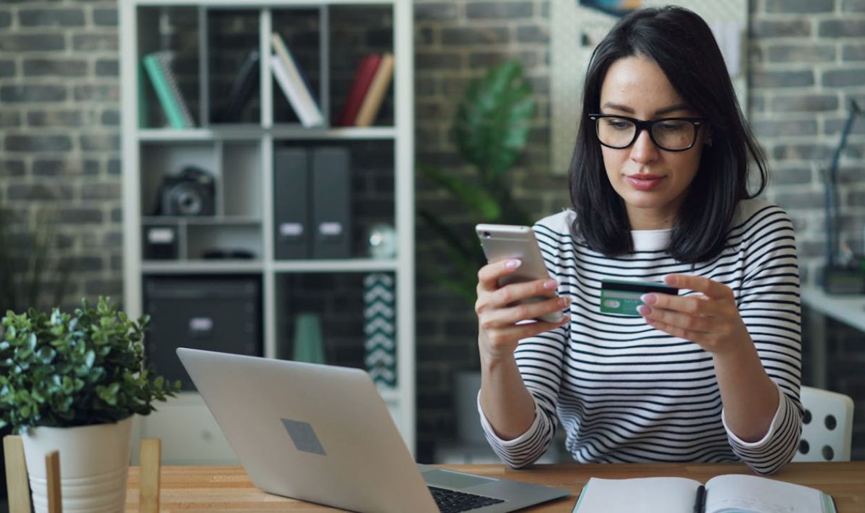 Woman Sitting in an Office and Holding a Smartphone and a Credit Card in her Hands