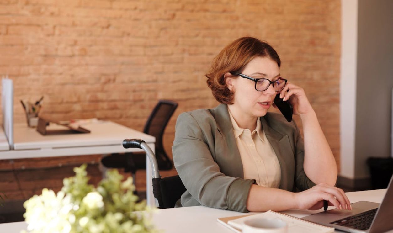 Photo of Woman Talking Through Smartphone While Using Laptop