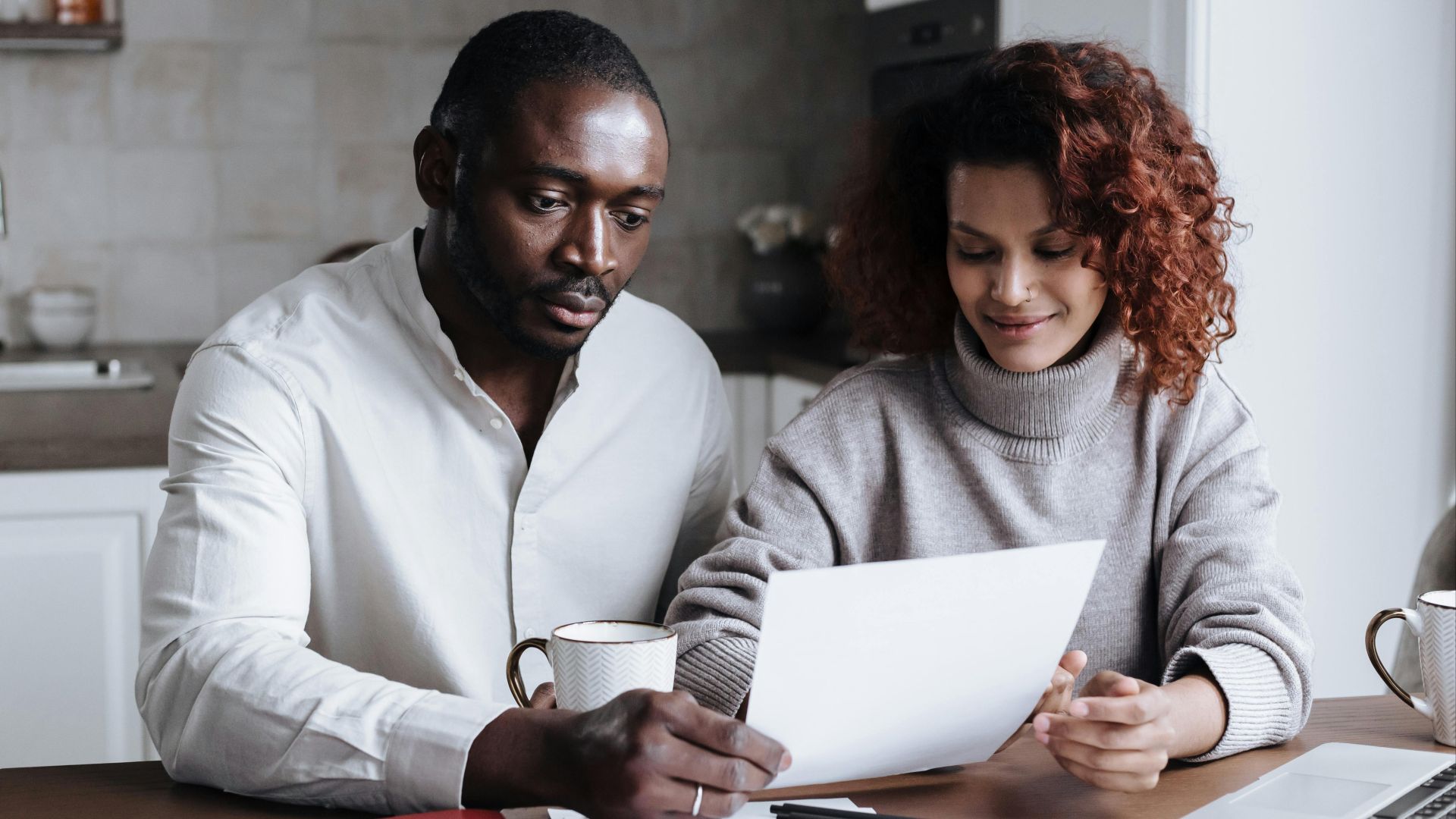 A couple reviews paperwork at a kitchen table, embodying teamwork and collaboration.