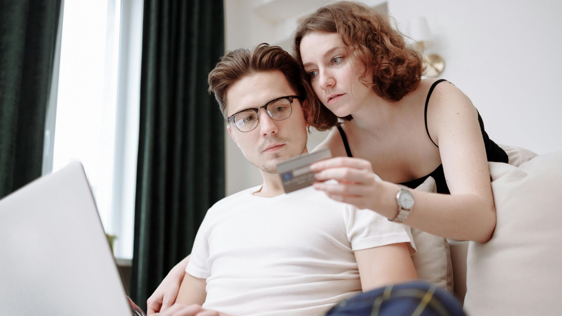A young couple using a laptop and credit card for online shopping indoors.