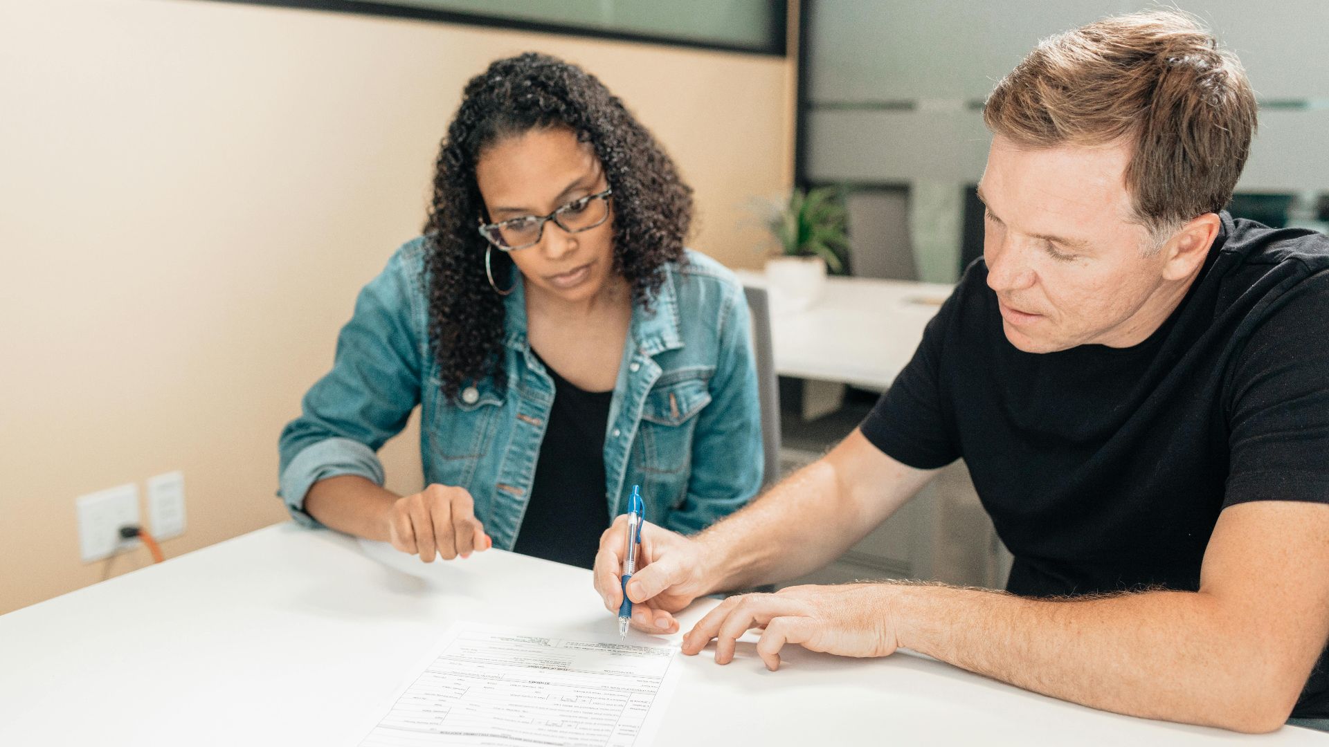 A couple working together to sign important legal documents at a desk in an office setting.