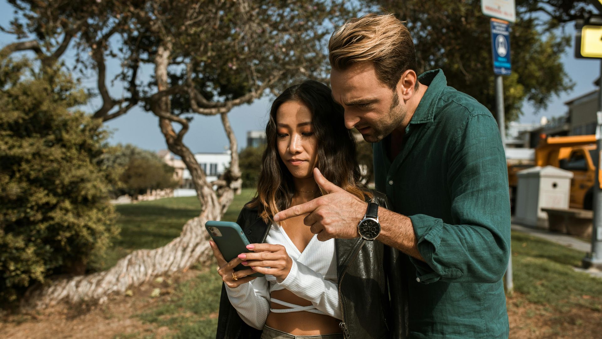 A man and woman using a smartphone together in a city park during daytime.