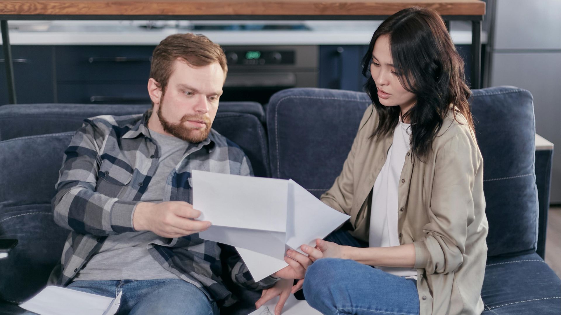 Asian woman and Caucasian man discussing taxes on couch.