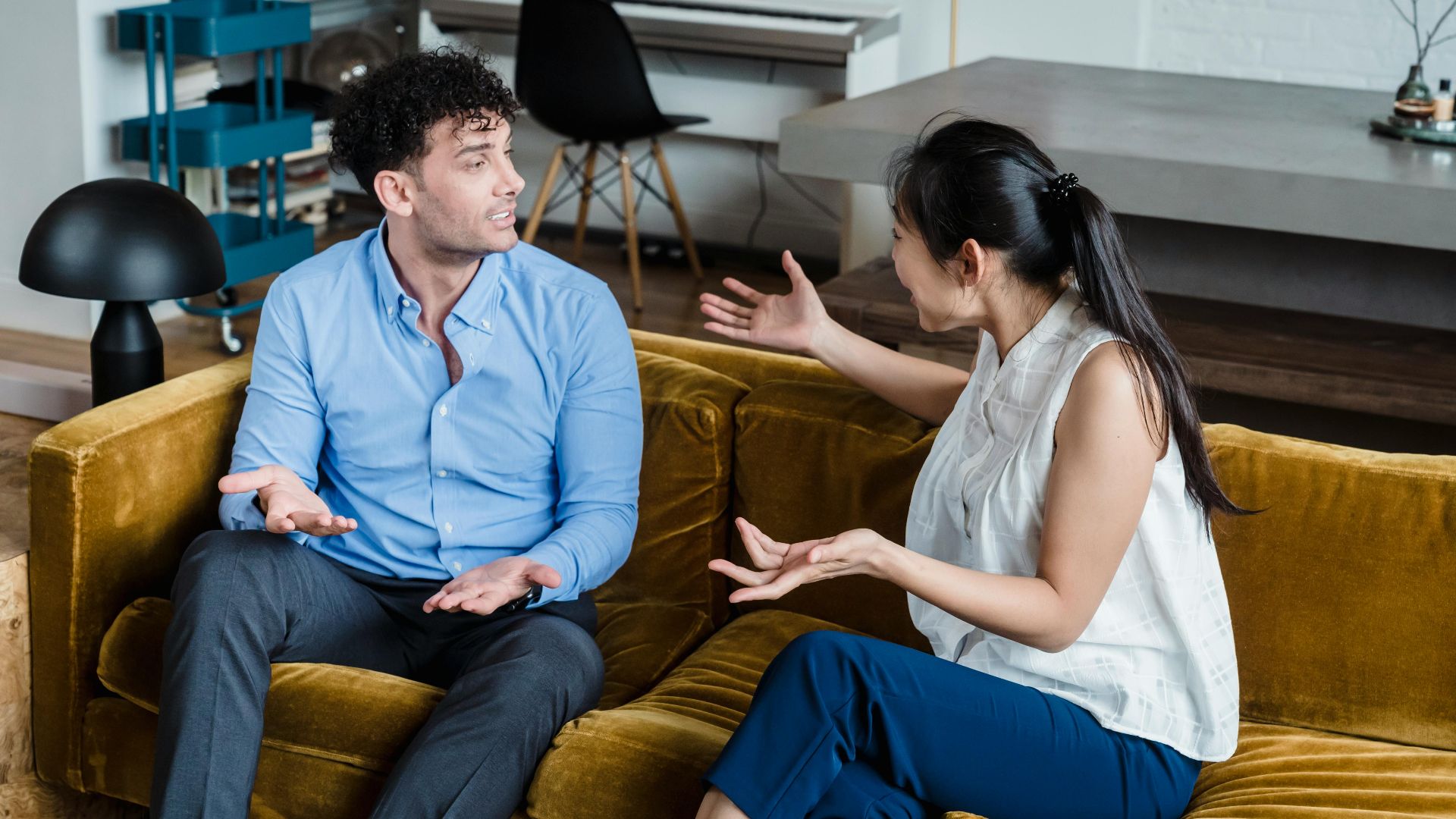 A man and woman engaged in an animated discussion while sitting on a sofa in a modern living room.