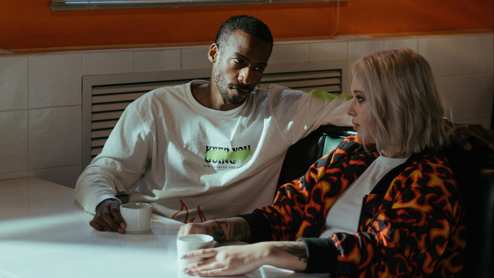 A couple converses over coffee in a cozy café, illuminated by soft daylight.
