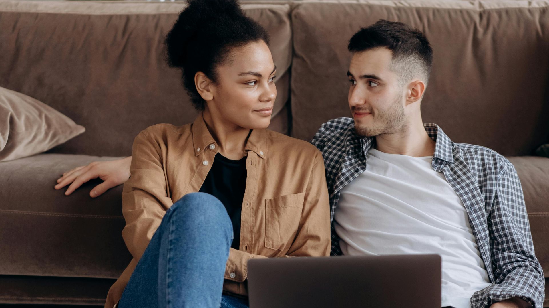 Couple sitting on floor with laptop, sharing a warm and cozy moment.