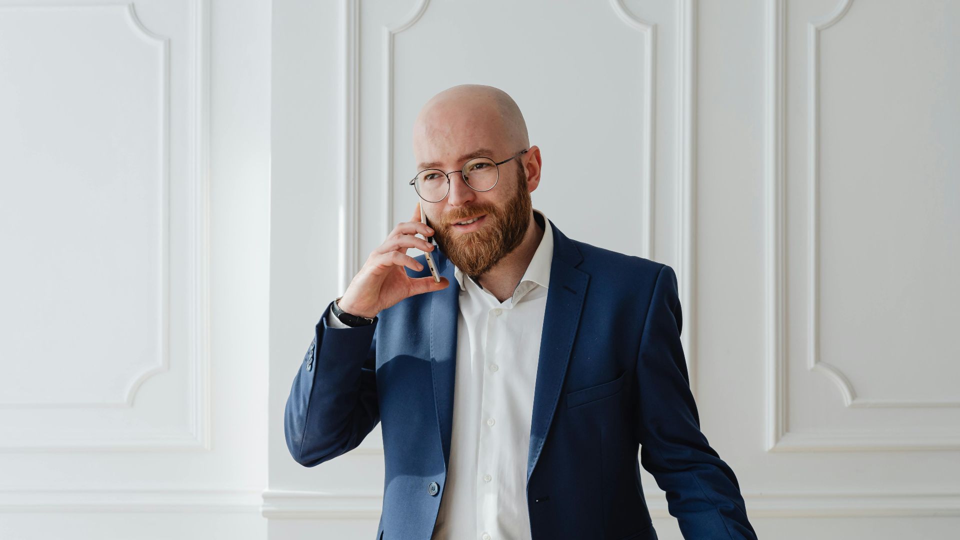 Bald bearded businessman in a suit having a phone call indoors.