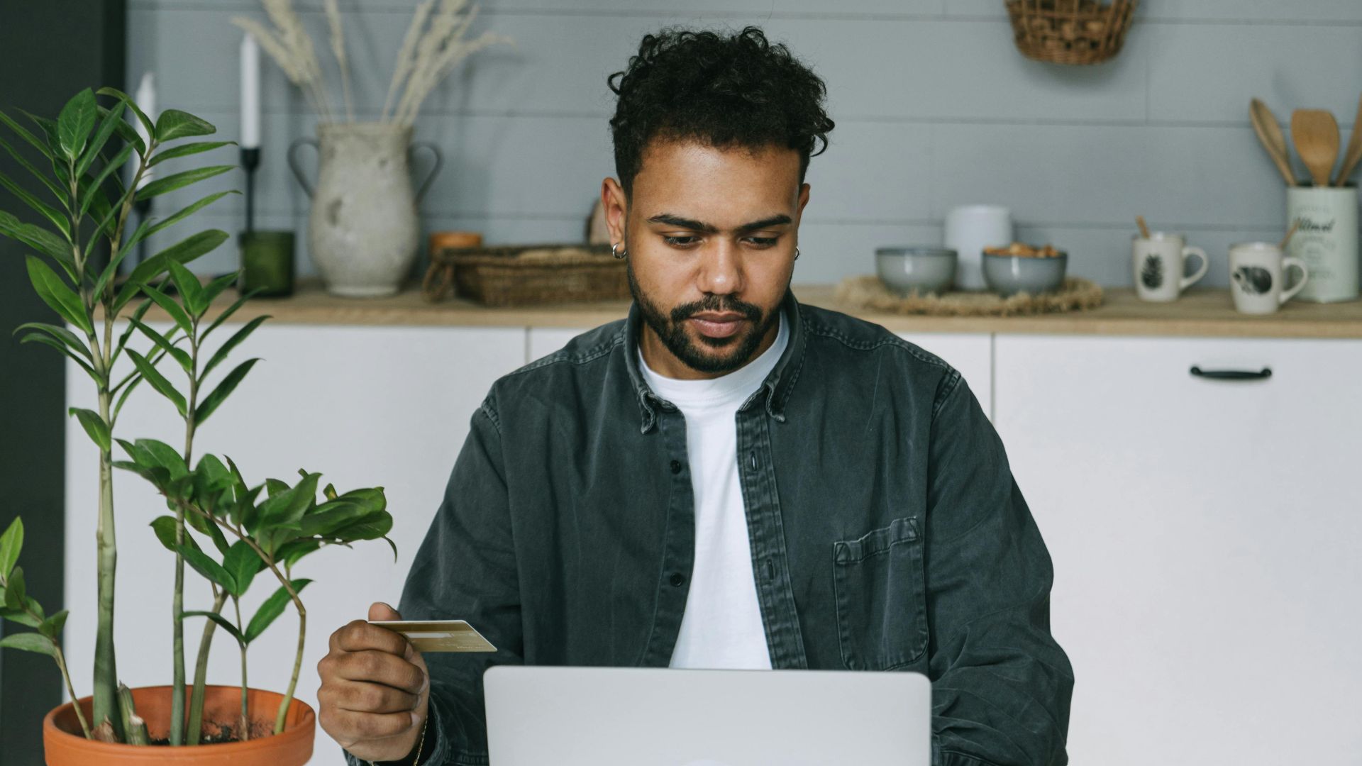A man using a laptop and credit card for online shopping in a cozy indoor setting.